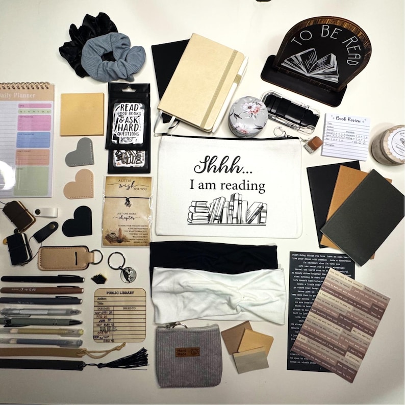 May include: A collection of reading and stationery items, including notebooks, pens, bookmarks, and a zippered pouch with the text "Shhh... I am reading." Also visible are scrunchies, headbands, and a wooden book stand.