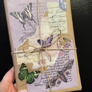May include: A brown paper package wrapped with twine and decorated with vintage-style butterfly and floral stickers. The package has handwritten text that reads "Possroid el pats M. Band Du Lorez Ziarrow."