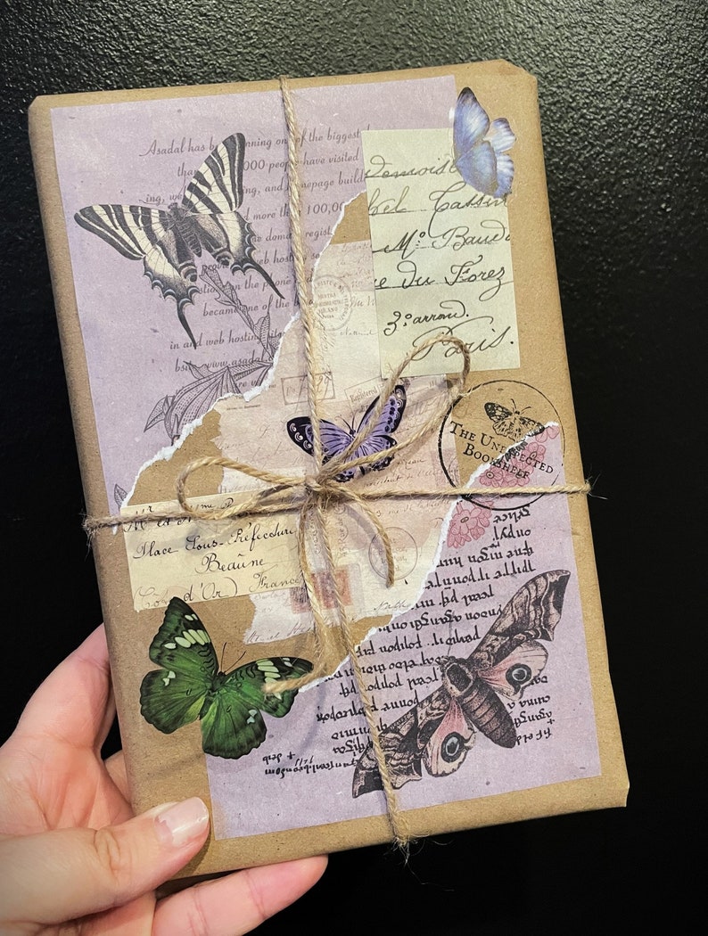 May include: A brown paper package wrapped with twine and decorated with vintage-style butterfly and floral stickers. The package has handwritten text that reads "Possroid el pats M. Band Du Lorez Ziarrow."