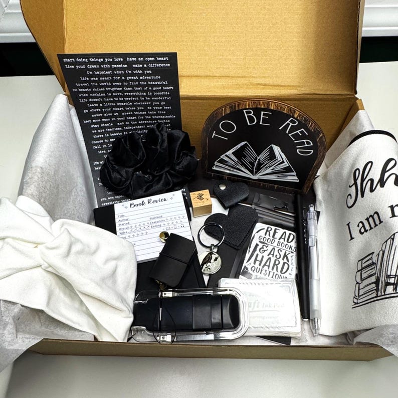 May include: A reading-themed gift box containing a black scrunchie, a wooden sign with "TO BE READ", a pen, a keychain, a notebook, and a canvas bag with the text "Shh I am reading". A perfect gift for book lovers.