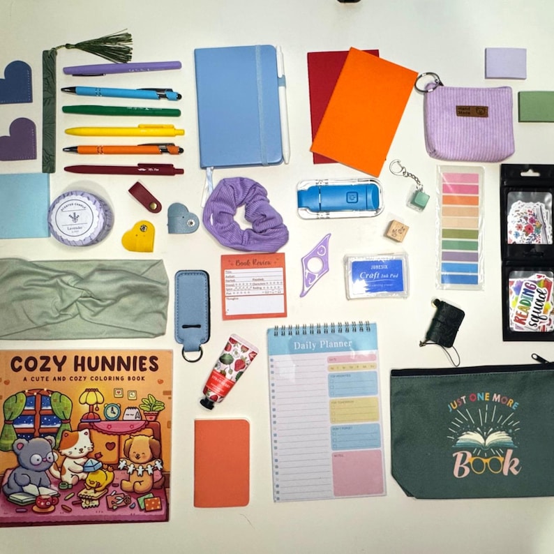 May include: A collection of stationery items and accessories, including pens, notebooks, a coloring book, a scrunchie, and a cosmetic bag. The items are in various colours, such as blue, orange, green, and purple. A green zippered pouch with the text "JUST ONE MORE Book" is also visible.