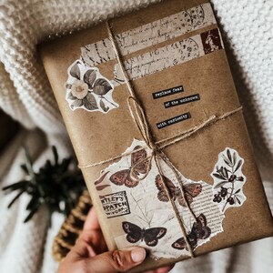May include: A brown paper package wrapped with twine and decorated with vintage stamps, paper scraps, and floral stickers. The package has a handwritten message that reads "replace fear of the unknown with curiosity".
