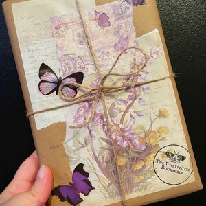 May include: A brown paper package wrapped with twine and decorated with purple and pink butterfly stickers, floral patterned paper, and a stamp that says "The Unexpected Bookshelf".