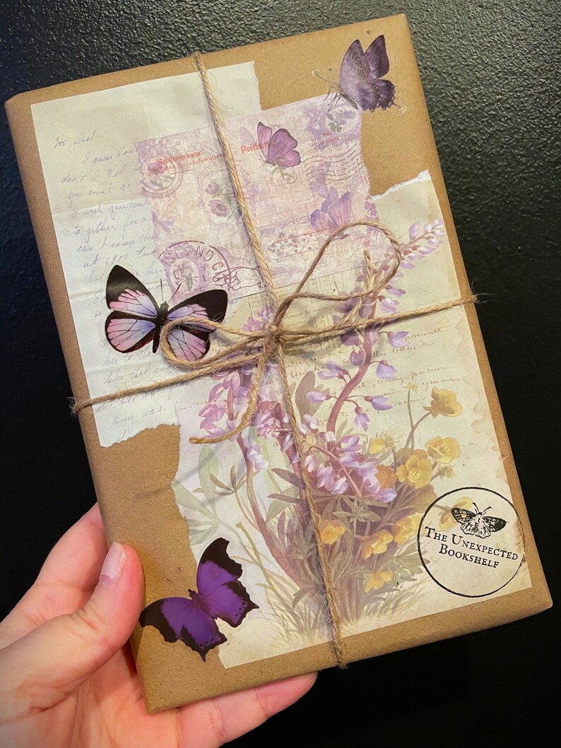 May include: A brown paper package wrapped with twine and decorated with purple and pink butterfly stickers, floral patterned paper, and a stamp that says "The Unexpected Bookshelf".