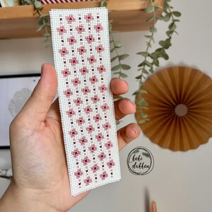 May include: A white bookmark with a pink and brown floral pattern. The bookmark is handmade and has the text "haki d&uuml;kkan" in a circle at the bottom.