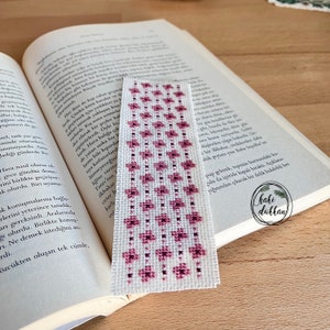 May include: A pink and white bookmark with a floral pattern. The bookmark is made of fabric and has a white background with pink flowers.