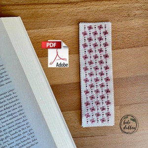 May include: A white bookmark with a pink and dark pink floral pattern. The bookmark has the text "haki dukkan" in the bottom right corner.