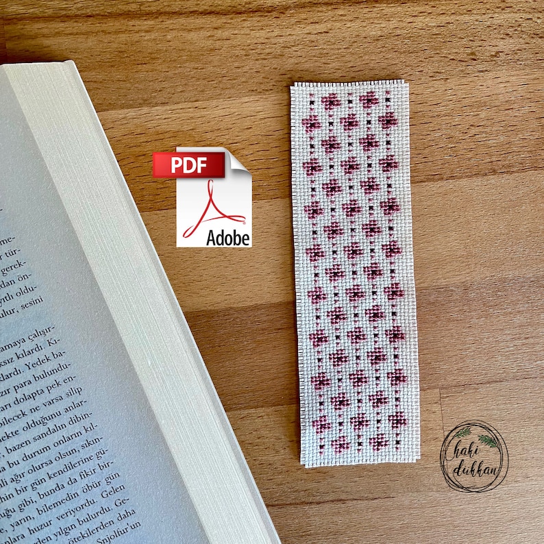 May include: A white bookmark with a pink and dark pink floral pattern. The bookmark has the text "haki dukkan" in the bottom right corner.