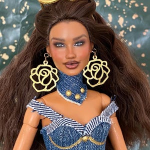 May include: A fashion doll with long brown hair, wearing gold rose-shaped earrings, a gold headband, and a blue denim off-the-shoulder top with a matching denim choker featuring gold studs. The doll has dark brown hair and detailed facial features.