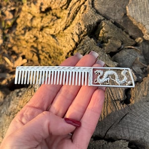 May include: A silver comb with a dragon design on the handle. The comb has fine teeth and is about 4 inches long.