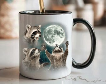 Può includere: Tazza in ceramica bianca con manico e bordo neri, con un design stravagante di procioni e luna piena. Sono raffigurati tre procioni, uno dei quali si protende verso la luna. La tazza viene probabilmente utilizzata per le bevande.