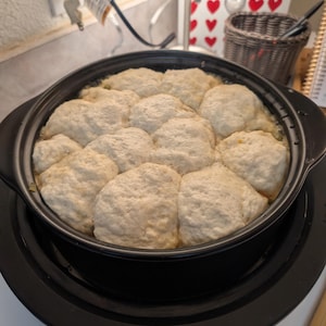 May include: A black slow cooker with a round, black ceramic insert filled with 10 fluffy, white biscuits.