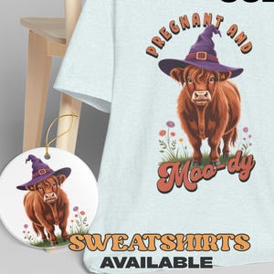 May include: Light blue sweatshirt with a graphic of a brown cow wearing a purple witch hat, with the text "Pregnant and Moo-dy". A matching ornament is also visible. The words "Colors More" and "Sweatshirts Available" are also displayed.