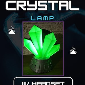 Puede incluir: Una lámpara de cristal verde con un soporte para auriculares. La lámpara está sobre una base negra y tiene un brillo verde.