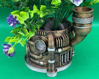 May include: A steampunk-style planter with a brown, metal, and silver finish. The planter has a pipe-like spout and a round base. It is filled with green plants and purple flowers.