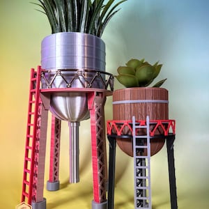 Könnte beinhalten: Zwei 3D-gedruckte Pflanztöpfe mit Leitern. Der größere Topf ist silberfarben mit einer roten Leiter und der kleinere Topf ist braun mit einer grauen Leiter. Beide Töpfe haben eine runde Form und stehen auf hohen, dünnen Beinen.