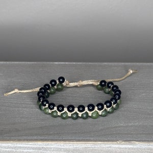 May include: A black and green beaded bracelet with a knotted cord closure.