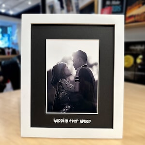 May include: A black and white photo of a couple in a white frame with a black mat. The couple is looking at each other and smiling. The text "happily ever after" is printed below the photo.