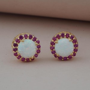 Pode incluir: Um par de brincos de ouro com uma pedra central de opala branca cercada por um halo de pedras preciosas cor-de-rosa.