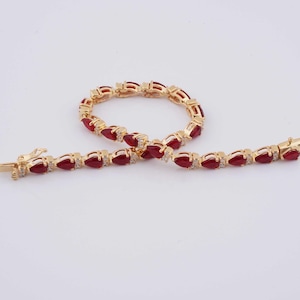 Puede incluir: Un brazalete de tono dorado con piedras rojas en forma de pera y detalles transparentes. El brazalete está hecho de dos piezas que se conectan con un cierre.