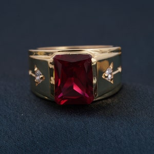 May include: A gold ring with a large, red, rectangular gemstone and two smaller, clear gemstones on the sides.