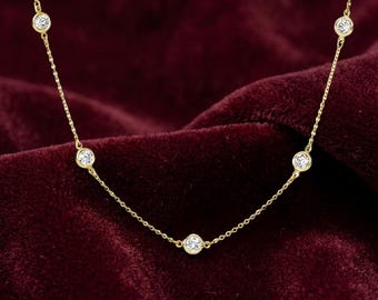 May include: A gold chain necklace featuring five evenly spaced, round, clear stones set in gold bezels. The delicate chain connects each stone, creating a station-style design that hangs in a gentle curve across the frame.