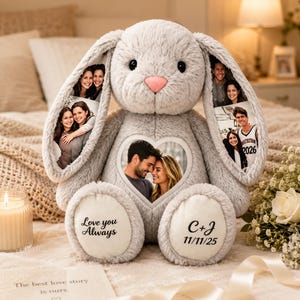 Puede incluir: Un conejo de peluche gris claro con un marco de fotos en forma de corazón en el pecho, fotos impresas en sus largas orejas y texto en sus pies que dice Love you Always y C+J 11/11/25. El peluche tiene una nariz rosa y textura suave.
