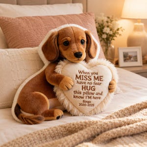 Puede incluir: Un peluche de perro salchicha marrón con orejas caídas, con una capa blanca con capucha, que sostiene un cojín en forma de corazón de color crema. El cojín presenta el texto bordado: When you MISS ME have no fear HUG this pillow and know I'M here Bingo 2020-2025.