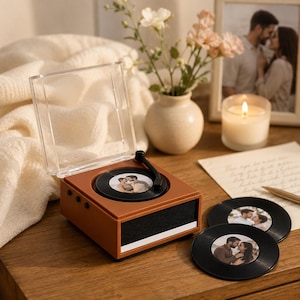 Peut inclure: Un lecteur de musique carré, marron et portable, doté d'un couvercle en plastique transparent et d'un bras de lecture noir. Le centre présente une photo circulaire d'un couple. Deux disques photo circulaires identiques sont posés à côté.