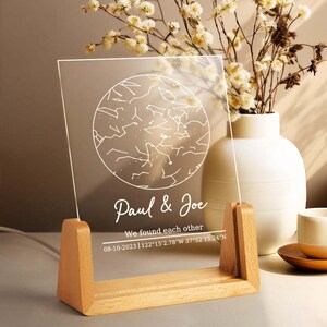Könnte beinhalten: Eine klare Acrylplatte mit einer weißen Sternenkarte und dem Text "Paul & Joe We found each other 08-10-2023 | 122°15′2.78"W 37°52′15.24"N" auf einem Holzständer.