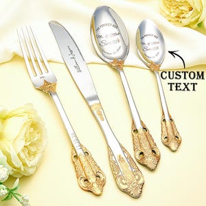 May include: A set of four gold-trimmed silverware pieces, including a fork, knife, and two spoons. The silverware is engraved with the text "The Perfect Mix" and "Mr. & Mrs. Smith" along with a date. The text "Custom Text" is also visible in the image.