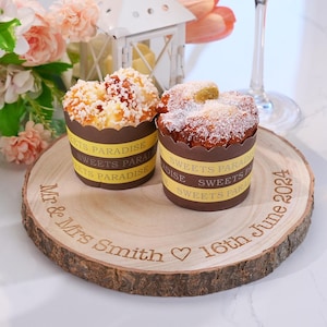 May include: Two small cakes with white frosting and sprinkles on a wooden round slice with the text "Mr. & Mrs. Smith ♥ 16th June 2024".