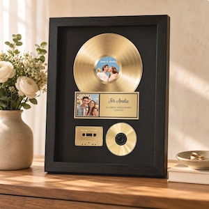 May include: A black framed wall display featuring a gold vinyl record with a central photo of a couple, a rectangular plaque with a photo and the text For Amelia YOU ARE MY WHOLE WORLD. I LOVE YOU, a gold cassette tape, and a gold compact disc.