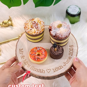 Puede incluir: Un soporte para pastel redondo de madera con un borde de corteza natural. El soporte tiene un mensaje grabado personalizado: "Mr. & Mrs. Smith ♥ 16th June 2024". El soporte está decorado con una dona, un postre de chocolate y dos pasteles pequeños.
