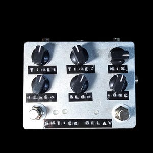 May include: Silver guitar effects pedal with six black knobs and two foot switches. The text on the pedal reads "TIME 1", "TIME 2", "MIX", "REGEN", "SLOW", "TONE", and "GUTIER DELAY".