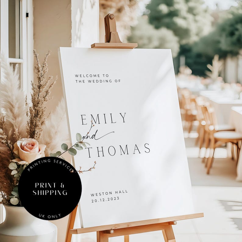 May include: White wedding welcome sign with black text that reads "Welcome to the wedding of Emily and Thomas, Weston Hall, 20.12.2023".