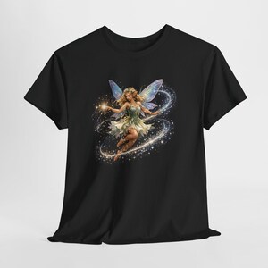 Pode incluir: Uma t-shirt preta com um gráfico central de uma fada com asas iridescentes e um vestido verde claro. A fada está rodeada por um rasto giratório de faíscas douradas brilhantes e luz, criando um efeito de movimento circular no tecido.