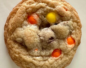May include: A close-up of a chocolate chip cookie with peanut butter M&Ms. The cookie is golden brown and has a slightly crispy texture. The M&Ms are scattered throughout the cookie, with some peeking out from the edges.