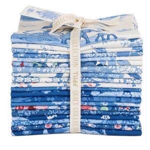May include: A stack of blue and white patterned fabric squares tied with a cream ribbon. The fabric features floral, elephant, and landscape designs. The ribbon is printed with the words "Tilda Quilt Collection".