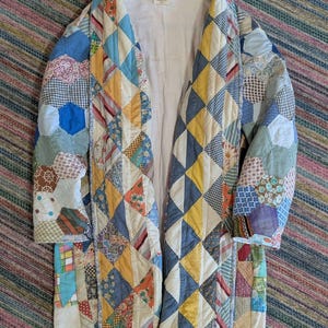 May include: A patchwork coat in a variety of colors, including blue, yellow, and white. The coat is made of various fabric patterns and shapes, creating a unique and vintage aesthetic. The coat is open in the front.