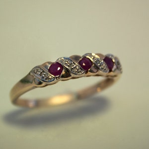 May include: A gold band ring with three red ruby stones and small white diamonds set in a twisted design.