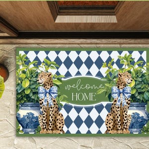 May include: Welcome home doormat with a blue and white diamond pattern, green foliage, and two cheetah figures with blue bows. The doormat has the text "welcome home" in a green oval.