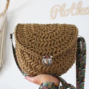 Peut inclure: Un sac à bandoulière en crochet marron avec un fermoir argenté et une bandoulière à motifs colorés.