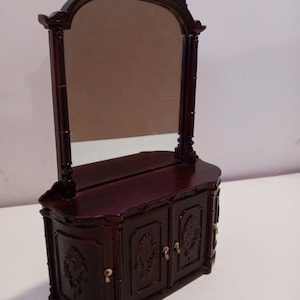 May include: A dark brown wooden vanity with a beveled mirror and three doors. The vanity has ornate carvings and gold-colored hardware.