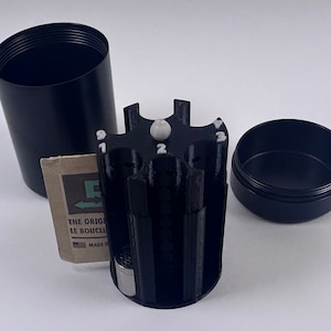 May include: Black metal container with a rotating, numbered, multi-compartment insert. The container is open and the insert is visible. The insert has numbers 1 through 9 on it. The container has a label that reads "The Original Le Bouchon Made in France".