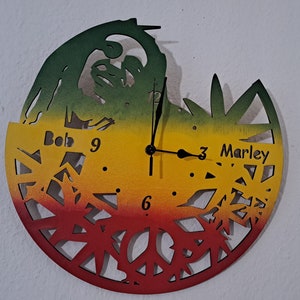 May include: A circular wooden clock with a red, yellow, and green gradient background. The clock face features a cutout design of a marijuana leaf and the words "Bob Marley" and "Bob 9".