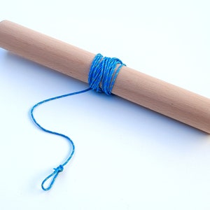 Può includere: Un bastoncino di legno con un cordoncino blu avvolto attorno. Il cordoncino ha un anello all'estremità.