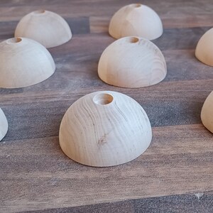 Peut inclure: Huit prises d'escalade en bois non finies, chacune avec un petit trou au centre. Les prises sont disposées en demi-cercle sur une surface en bois.