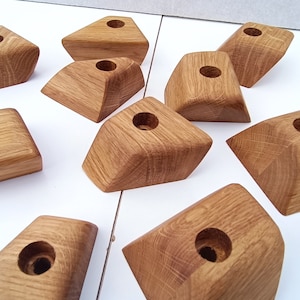 Könnte beinhalten: Eine Sammlung von zehn hölzernen Kerzenhaltern. Jeder Halter hat eine geometrische Form mit einer kreisförmigen Vertiefung oben. Das Holz hat eine natürliche, hellbraune Farbe und sichtbare Maserung.