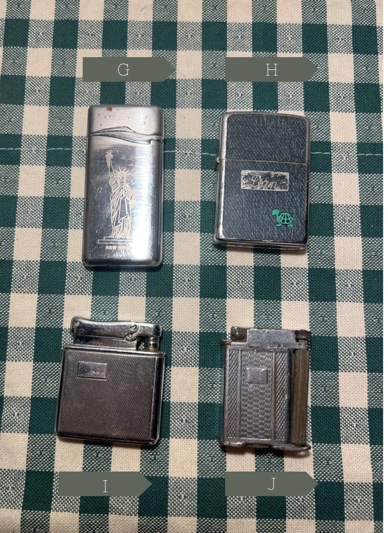 May include: Four silver lighters on a green and white checkered background. The lighters have different designs, including a Statue of Liberty, a turtle, and two with geometric patterns.